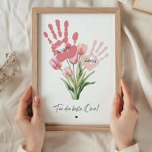 May include: A framed print with pink handprints and the names Liam and Lena. The handprints are arranged to look like a bouquet of pink tulips. The text "For the best Oma!" is at the bottom of the print.