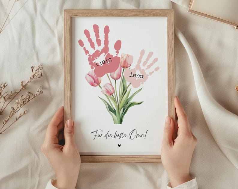 May include: A framed print with pink handprints and the names Liam and Lena. The handprints are arranged to look like a bouquet of pink tulips. The text "For the best Oma!" is at the bottom of the print.