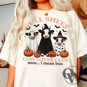 May include: White t-shirt with a graphic of three cows dressed in Halloween costumes. The cows are wearing a ghost costume, a witch costume, and a vampire costume. The text "Full Sheet Cow Lover Club moo... i mean boo" is printed below the cows.