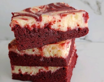 May include: A stack of three red velvet cheesecake bars with a swirl of cream cheese frosting. The bars are layered on top of each other and have a rich, red color.