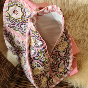 Puede incluir: Bolso tote con estampado rosa y blanco con un dise&ntilde;o floral en negro, rosa y amarillo. Tiene cierre de cremallera y una correa rosa. El interior es blanco. El bolso es de tela y tiene un estampado de cuadros en los laterales.