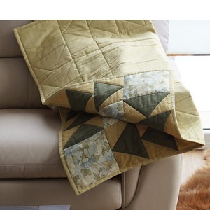 Pode incluir: Uma colcha de retalhos bege e verde com um padr&atilde;o floral. A colcha est&aacute; dobrada e drapeada sobre um sof&aacute; bege.