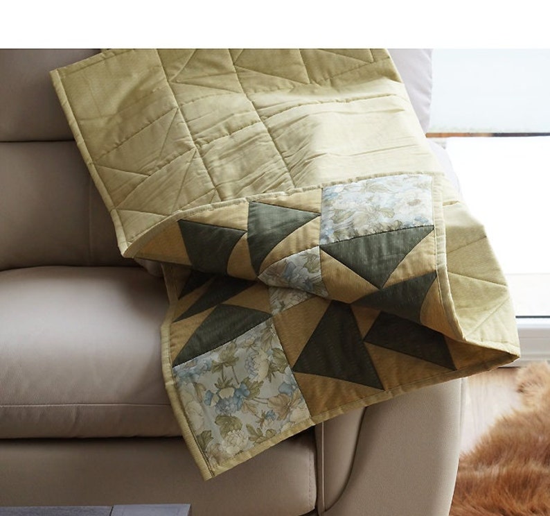 Pode incluir: Uma colcha de retalhos bege e verde com um padr&atilde;o floral. A colcha est&aacute; dobrada e drapeada sobre um sof&aacute; bege.