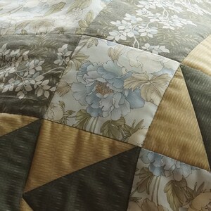 Pode incluir: Um cobertor de retalhos com um padr&atilde;o geom&eacute;trico de tri&acirc;ngulos e quadrados. O cobertor &eacute; feito de diferentes tecidos com estampas florais em tons de verde, marrom e azul.