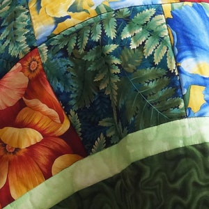 May include: Close-up of a patchwork quilt with floral and fern patterns. The quilt features vibrant colors, including red, orange, yellow, blue, and green. The design incorporates large flower motifs and detailed fern leaves.