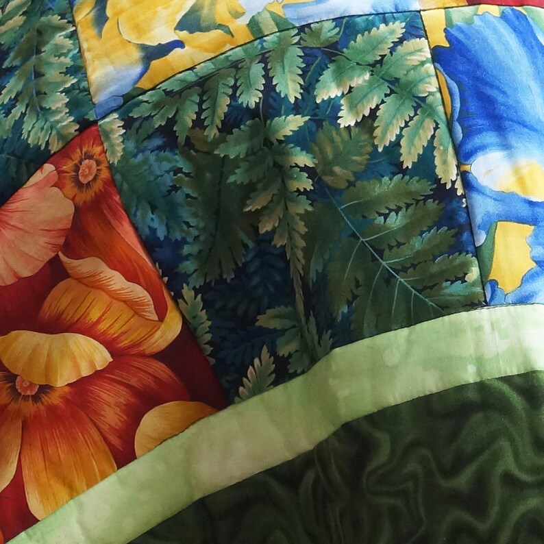 May include: Close-up of a patchwork quilt with floral and fern patterns. The quilt features vibrant colors, including red, orange, yellow, blue, and green. The design incorporates large flower motifs and detailed fern leaves.