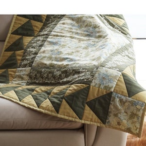 Pode incluir: Um cobertor de retalhos verde e amarelo com um padr&atilde;o floral. O cobertor est&aacute; dobrado e drapeado sobre um sof&aacute;.