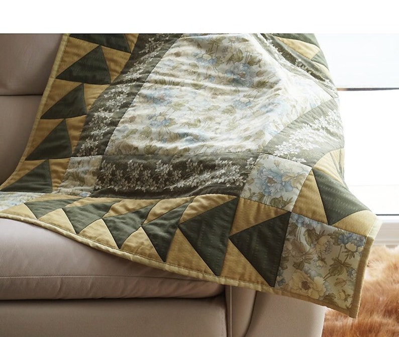 Pode incluir: Um cobertor de retalhos verde e amarelo com um padr&atilde;o floral. O cobertor est&aacute; dobrado e drapeado sobre um sof&aacute;.