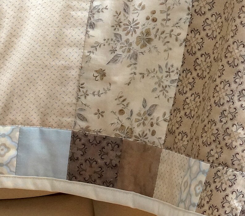 Pode incluir: Um edredom de patchwork com v&aacute;rios tecidos estampados em tons de bege, castanho e azul. O edredom incorpora desenhos florais, pontilhados e geom&eacute;tricos, criando uma est&eacute;tica vintage. As bordas s&atilde;o finalizadas com uma borda branca.