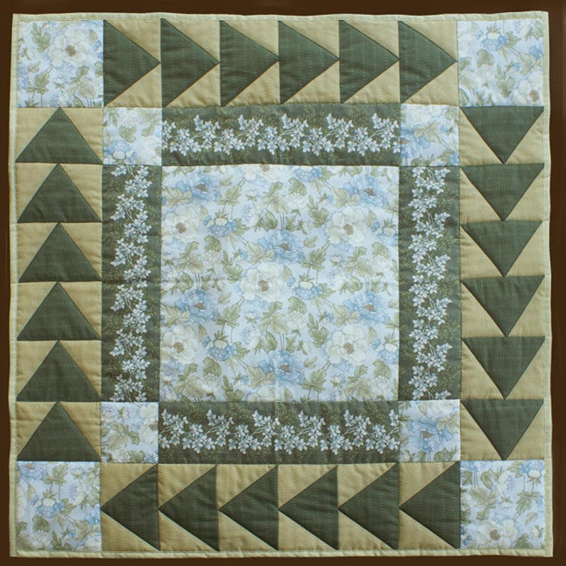 Pode incluir: Uma colcha de retalhos verde e bege com um padr&atilde;o floral no centro. A colcha &eacute; feita de quadrados e tri&acirc;ngulos.