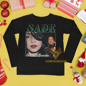 May include: Black long-sleeve t-shirt with a graphic print of Sade, a singer, with the text "SADE" and "Sweetest Operator" on the front.