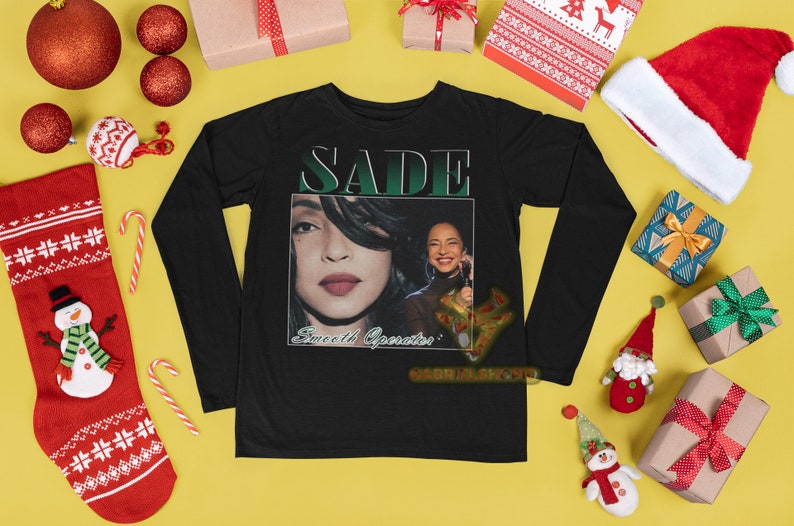 May include: Black long-sleeve t-shirt with a graphic print of Sade, a singer, with the text "SADE" and "Sweetest Operator" on the front.