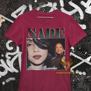 May include: A maroon t-shirt with a vintage-style graphic of Sade, a singer, with the text "SADE" and "Smooth Operator" printed on the front.