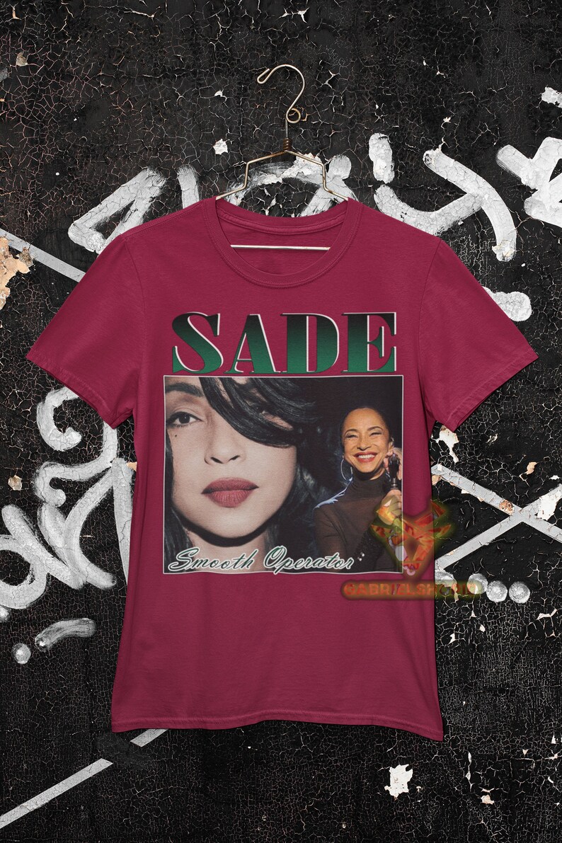 May include: A maroon t-shirt with a vintage-style graphic of Sade, a singer, with the text "SADE" and "Smooth Operator" printed on the front.