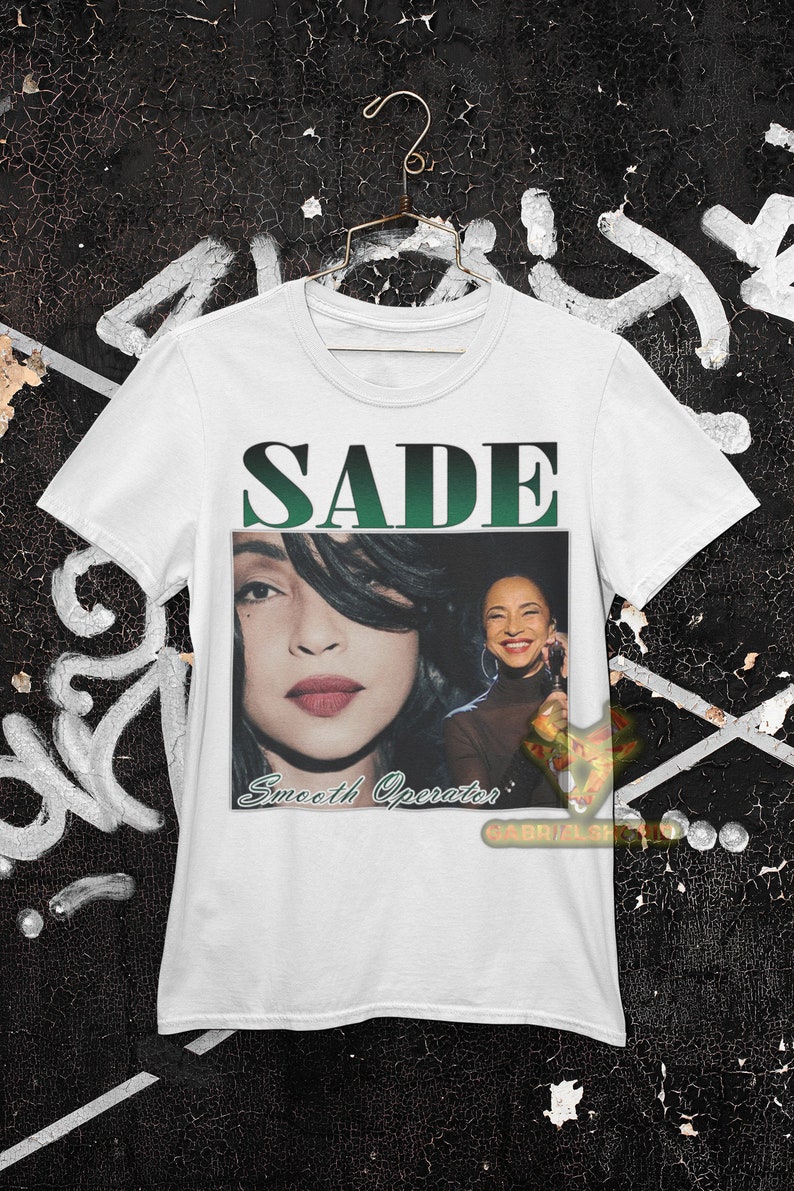 May include: White t-shirt with a green and black graphic of Sade with the text "SADE" and "Smooth Operator" printed on the front.