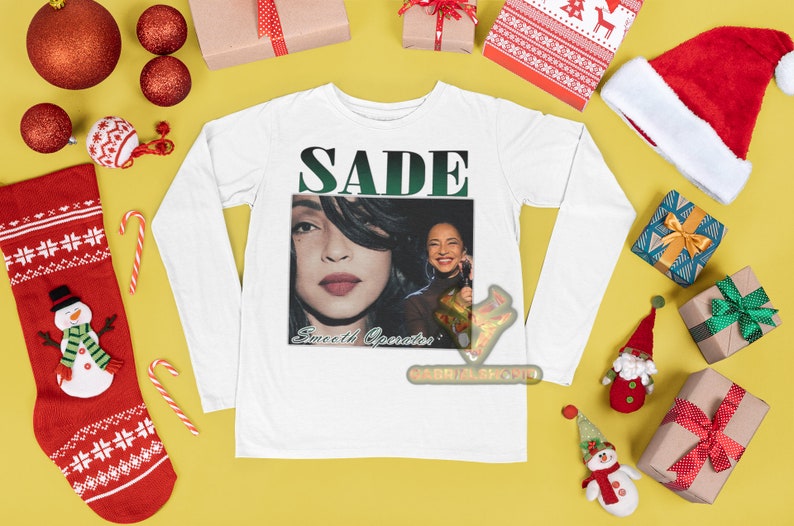 May include: White long-sleeve shirt with a graphic print of Sade, a singer, with the text "SADE" and "Sweetest Operator" on the front.