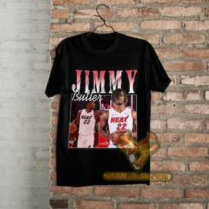 May include: Black t-shirt with a vintage-style graphic of basketball player Jimmy Butler wearing a Miami Heat jersey with the number 22. The text "JIMMY Butler" is printed in white above the image.
