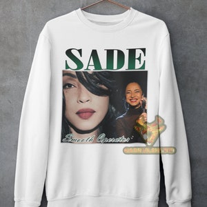 May include: White sweatshirt with a green and black graphic print of Sade. The graphic includes a photo of Sade and the text "SADE" and "Smooth Operator".