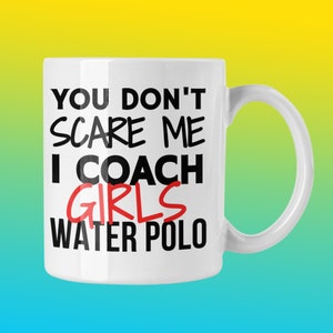 Può includere: Una tazza da caffè in ceramica bianca con testo nero che recita "You don't scare me I coach girls water polo". La parola "girls" è in rosso.