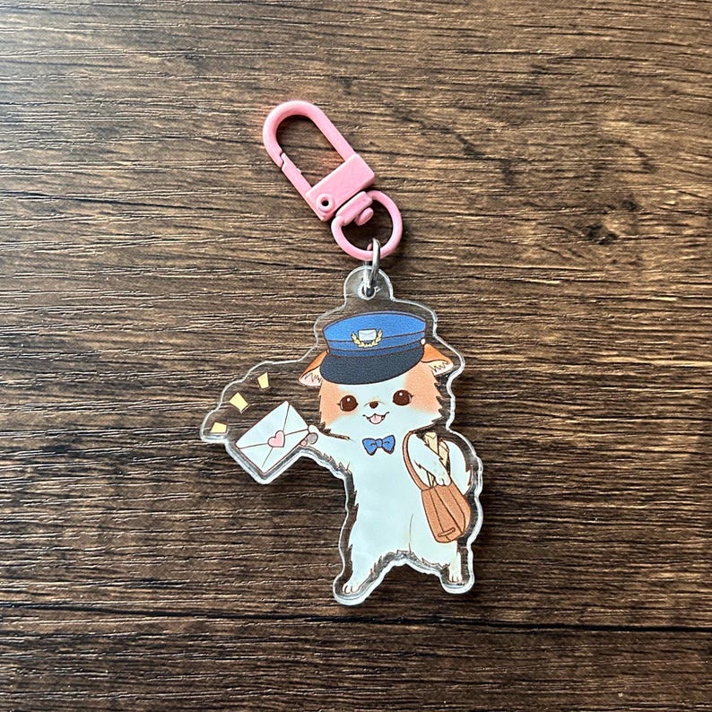 May include: A clear acrylic keyring featuring a cartoon cat dressed as a postman. The cat wears a blue hat and carries a mailbag and an envelope with a heart. The keyring has a pink clasp.