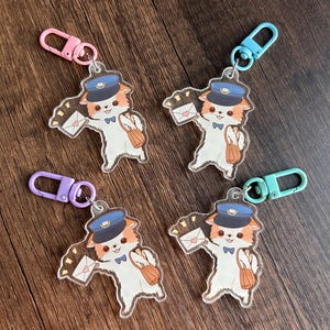 May include: Four clear acrylic keychains depicting a cartoon cat as a postman. The cat wears a blue hat and bow tie, carrying a mailbag and an envelope with a heart. Each keychain has a different coloured clasp.