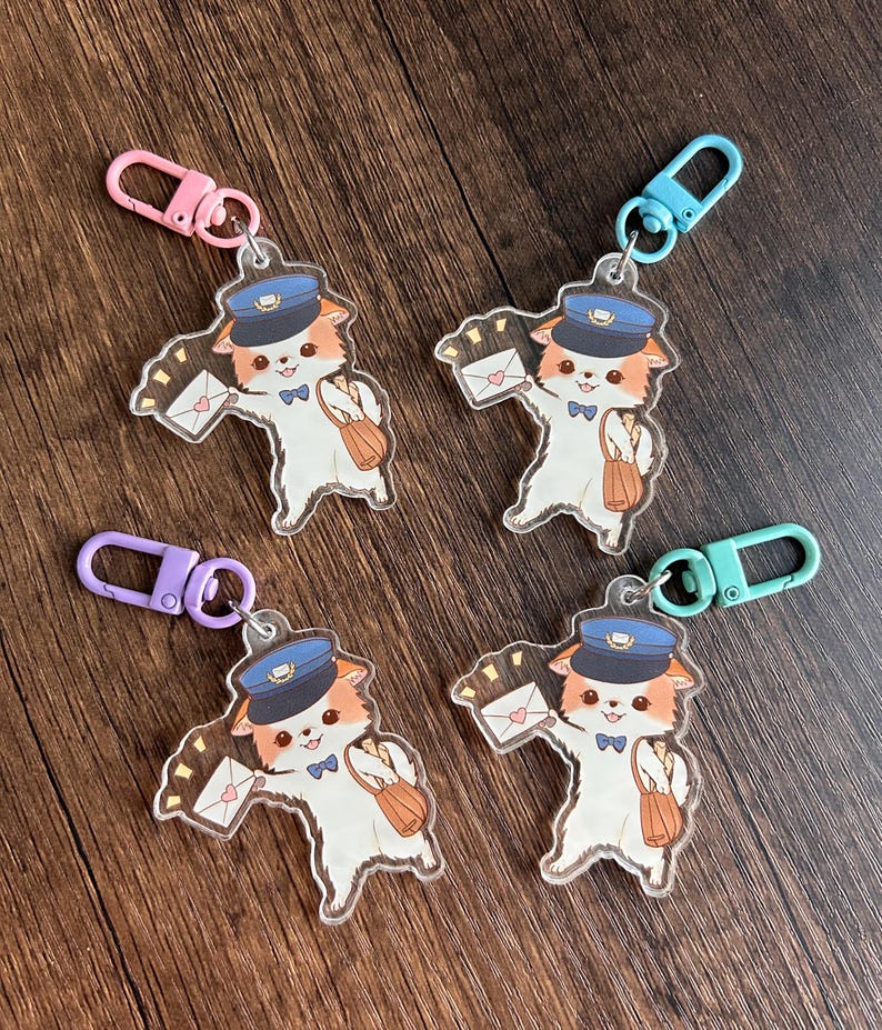 May include: Four clear acrylic keychains depicting a cartoon cat as a postman. The cat wears a blue hat and bow tie, carrying a mailbag and an envelope with a heart. Each keychain has a different coloured clasp.