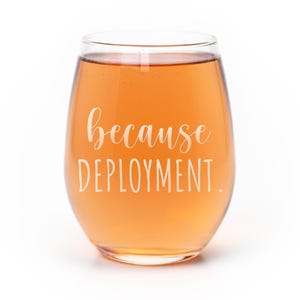 May include: A stemless wine glass filled with a light orange liquid. The glass features white text printed on the front that reads because DEPLOYMENT. The design uses a combination of a cursive script font and a simple sans-serif typeface.