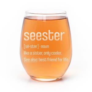 May include: A stemless wine glass filled with an amber-colored liquid. The glass features white printed text that reads: seester [sē-stər] - noun like a sister, only cooler. See also: best friend for life.