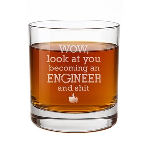 May include: A clear glass tumbler filled with an amber-colored liquid. The front of the glass features white etched text that reads: WOW, look at you becoming an ENGINEER and shit, accompanied by a small graphic of a thumbs-up icon below the text.