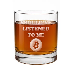 May include: A clear glass tumbler filled with an amber-colored liquid. The front of the glass features the etched white text SHOULD'VE LISTENED TO ME positioned above a circular Bitcoin symbol icon, creating a distinct contrast against the liquid.