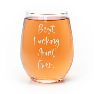 May include: A clear, stemless wine glass filled with a light amber liquid. The glass features white, cursive-style text that reads: Best F*cking Aunt Ever., with a small heart symbol replacing the asterisk in the word F*cking.