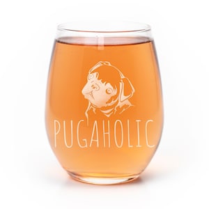 May include: A clear stemless wine glass filled with a light orange liquid. The glass features an etched white graphic of a pug dog head positioned above the text PUGAHOLIC in a simple, clean, sans-serif font centered on the front of the glass.