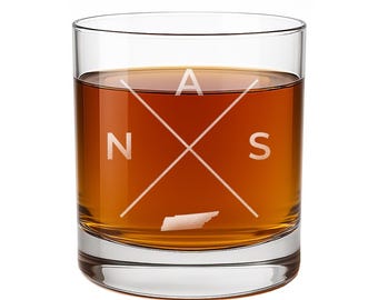 May include: A clear glass tumbler filled with amber liquid, featuring an etched design of two intersecting diagonal lines forming an X. The letters N, A, and S are positioned between the lines, with a small outline of Tennessee at the bottom.