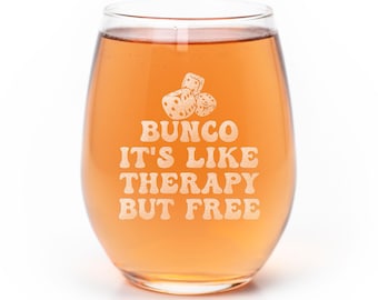 May include: A clear stemless wine glass filled with an amber-colored liquid. The glass features an etched design of three dice above the text BUNCO IT'S LIKE THERAPY BUT FREE in a bold, rounded font centered on the front of the glass.
