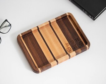 May include: Rectangular wooden serving tray with alternating dark and light wood stripes. The tray has a raised edge and engraved initials, a heart, a soccer ball, and a paw print. The tray is on a white surface.