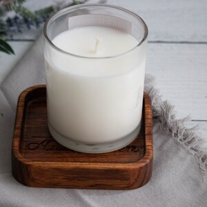 May include: A white candle in a clear glass jar sits on a wooden coaster with the word "Love" engraved on it.