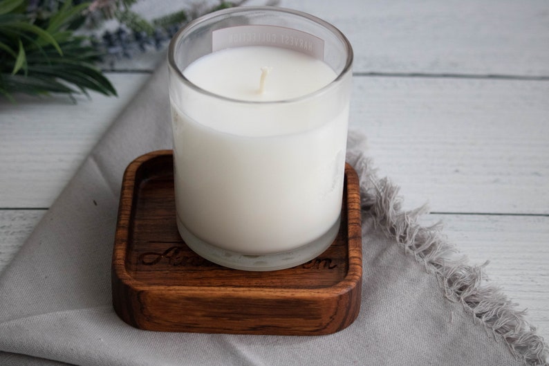 May include: A white candle in a clear glass jar sits on a wooden coaster with the word "Love" engraved on it.