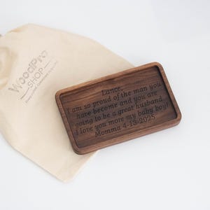Op de afbeelding: Een houten dienblad met een gegraveerde persoonlijke boodschap op het oppervlak. De boodschap luidt "Lance, ik ben zo trots op de man die je bent geworden en je zult een geweldige echtgenoot zijn. Ik hou nog meer van je, mijn kleine jongen! Mama 4-13-2025".