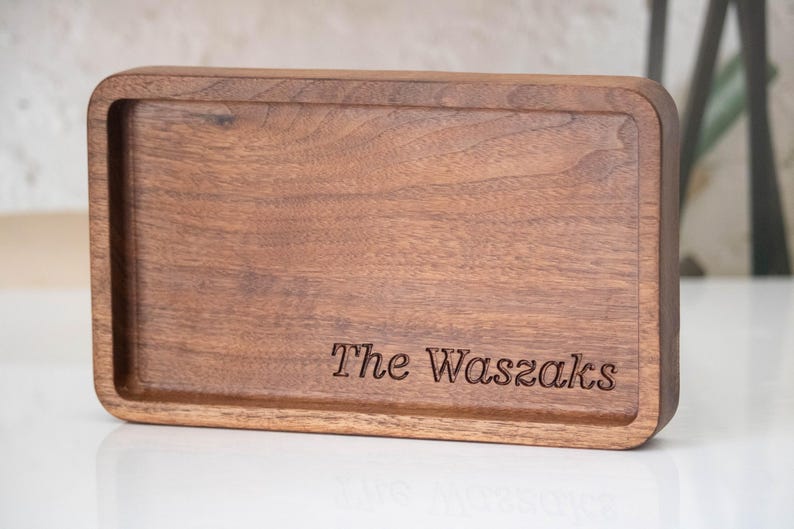 May include: A rectangular wooden tray with rounded corners. The tray is made of dark brown wood and has a recessed interior. The words "The Waszaks" are engraved on the tray's surface.