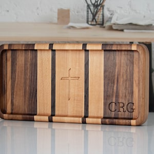 May include: A rectangular wooden serving tray with a cross design and the initials "CRG" engraved on the surface. The tray is made of light and dark wood.