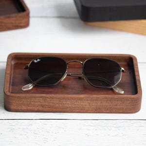 A handcrafted rectangular wooden catchall tray with a smooth finish, holding a pair of sunglasses. The tray has a minimalist design and is made from walnut  hardwood.