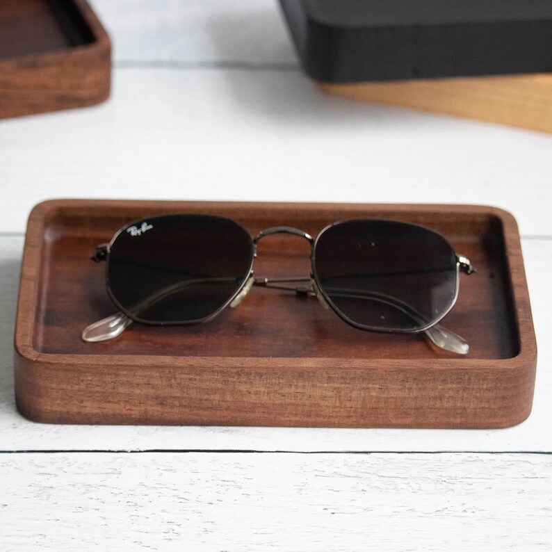 A handcrafted rectangular wooden catchall tray with a smooth finish, holding a pair of sunglasses. The tray has a minimalist design and is made from walnut  hardwood.