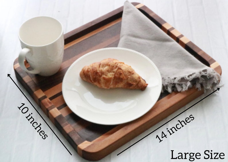 Op de afbeelding: Een houten dienblad met een natuurlijke houten afwerking. Het dienblad is 35,56 cm lang en 25,4 cm breed. Het heeft een veelkleurig houten ontwerp met een lichtgrijze servet erop. Het dienblad is groot genoeg om een bord, een kopje en een croissant te houden.