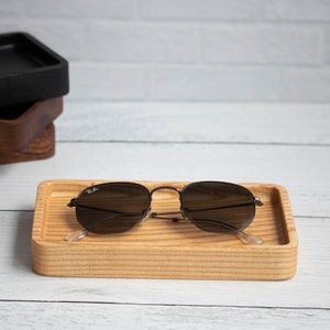 May include: A wooden tray with a light brown finish and a pair of sunglasses resting on top. The sunglasses have a dark brown frame and lenses.