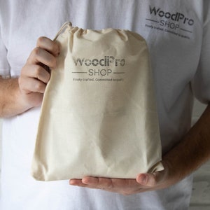 Op de afbeelding: Een persoon die een witte canvas tas vasthoudt met de tekst "WoodPro Shop" en de slogan "Finely crafted. Committed to quality."