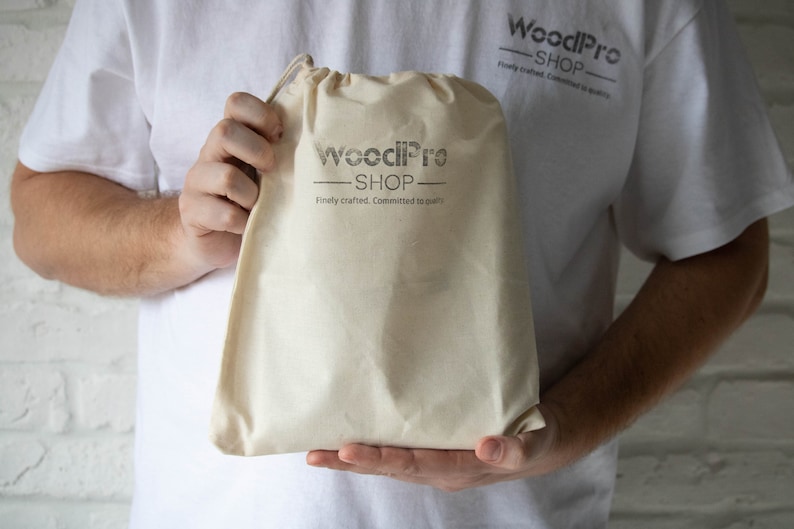 Op de afbeelding: Een persoon die een witte canvas tas vasthoudt met de tekst "WoodPro Shop" en de slogan "Finely crafted. Committed to quality."