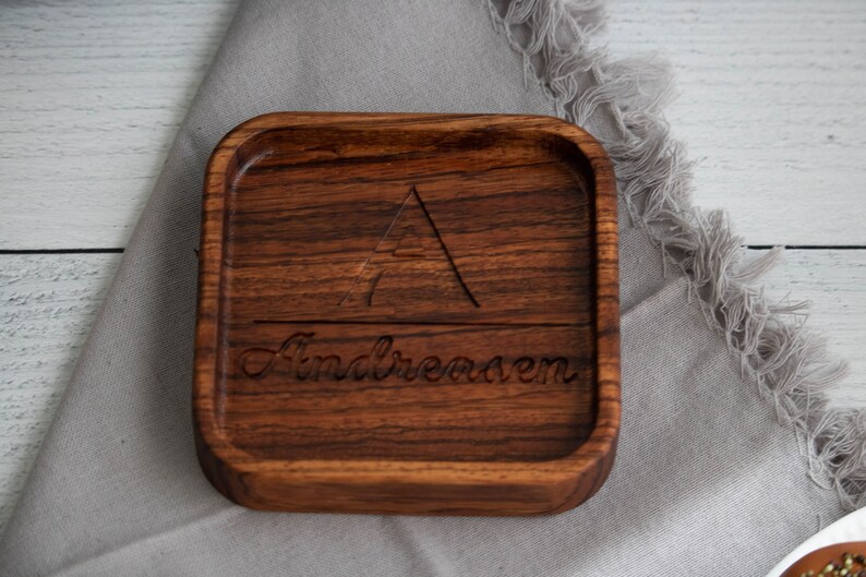 May include: A square wooden tray with a carved triangle and the name "Andreasen" engraved on the surface. The tray is made of dark wood and has a natural finish.