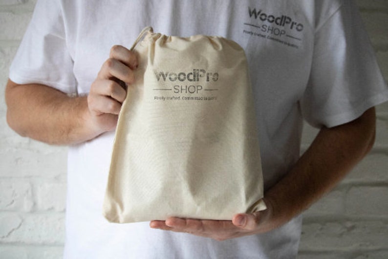 May include: A beige drawstring bag held by a person. The bag has the text "WoodPro SHOP" printed on it in gray, along with the tagline "Finely crafted. Committed to quality."