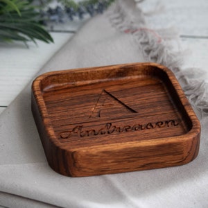 May include: A small, square wooden tray with a dark brown stain. The tray has a triangle and the name "Andreasen" carved into the wood.