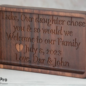 May include: A wooden plaque with a personalized message that reads "Luke, Our daughter chose you & so would we Welcome to our Family July 8, 2023 Love, Dar & John".